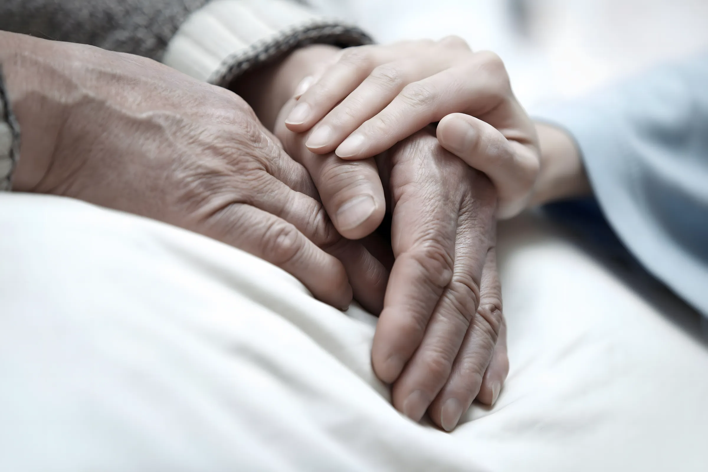 Eine jüngere Person hält behutsam die Hand eines älteren Menschen.